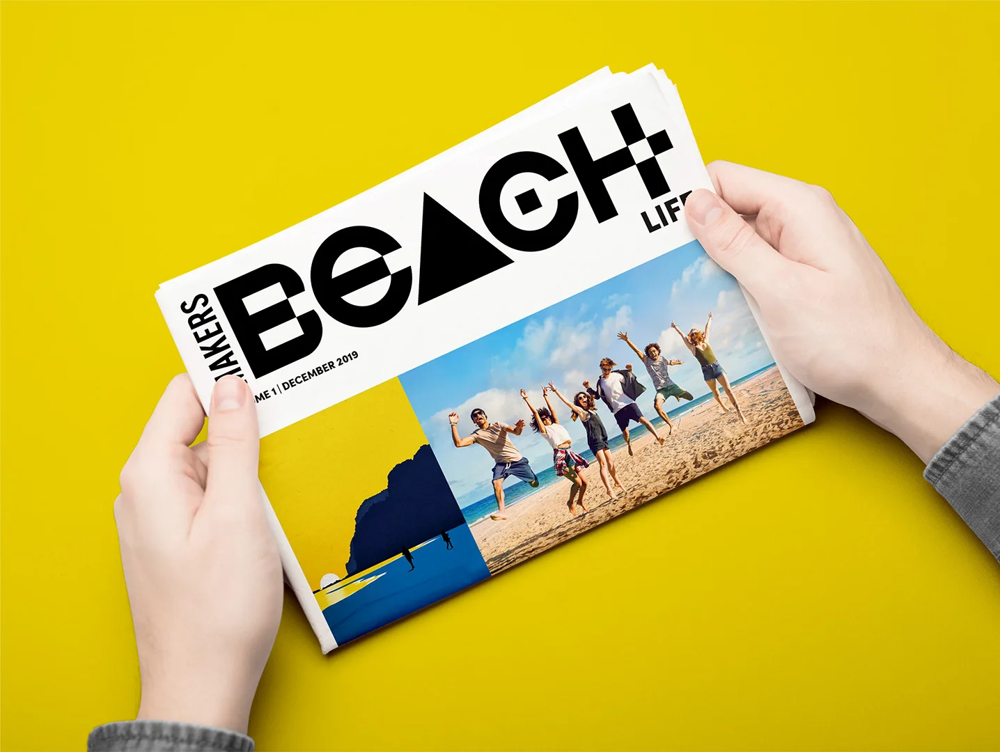 Hands holding the printed Makers Beach ‘Beach Life’ tabloid, Volume 1, December 2019, with the wordmark and beach photography on the cover